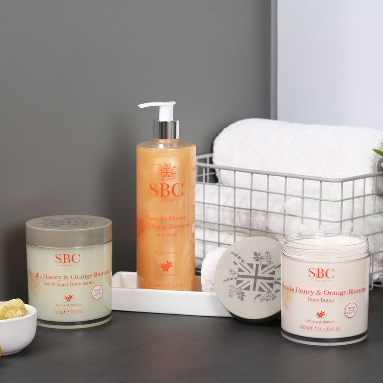 Manuka Honey & Orange Blossom Scrub, Body Wash and Body Butter in a bathroom with towels and honey comb