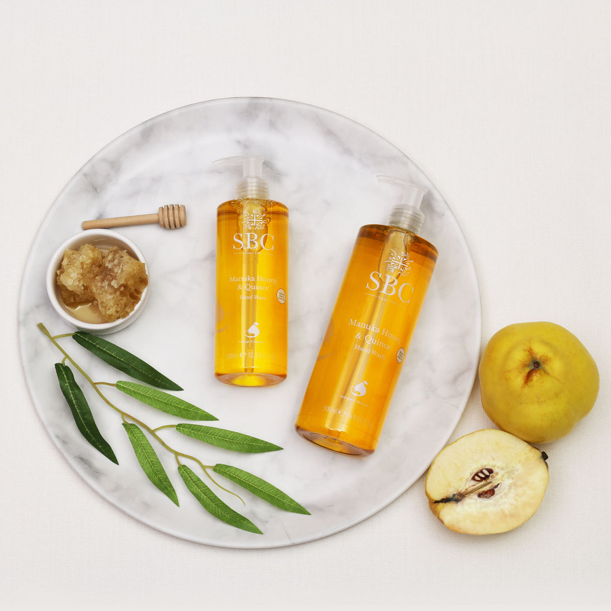 300ml and 500ml Manuka Honey & Quince Hand Wash on a marble plate with honey comb,, leaves and Quinces 